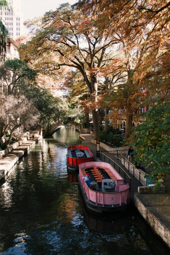 Charming boats along San Antonio River Walk with vibrant autumn foliage and urban scenery.