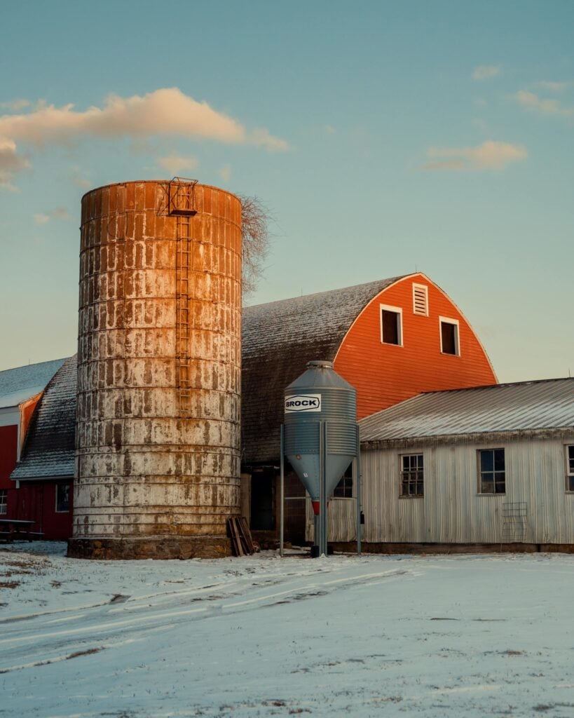 Rustic farm scene in Connecticut during golden hour with snow, barn, and silo.