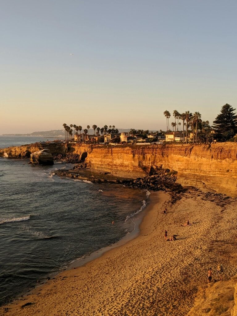 Serene sunset view of San Diego cliffs, beach, and sea with palm trees and golden sand.