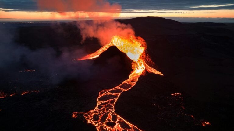 A breathtaking view of an erupting volcano with flowing lava at twilight, showcasing nature's power.