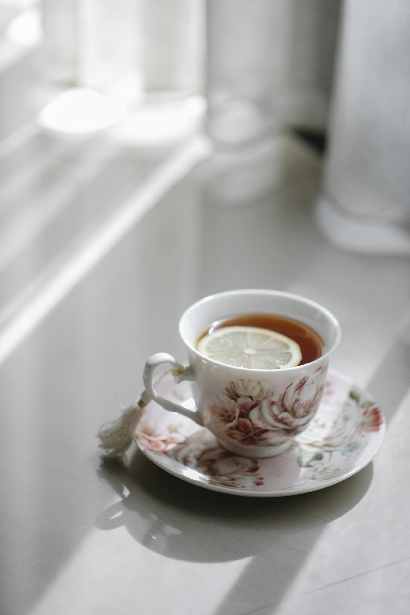 A delicate floral teacup with a lemon slice, bathed in soft sunlight on a sunny afternoon.