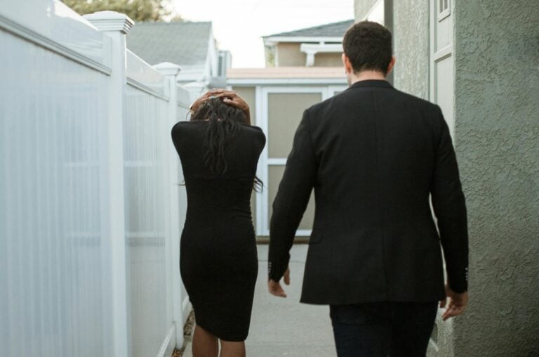 Back view of an interracial couple walking apart in an alley, suggesting breakup tension.