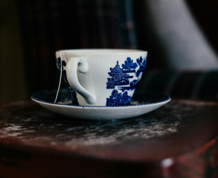 Ceramic white cup with blue pictures standing on saucer on wooden surface in room
